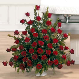 Large fan-shaped arrangement of red roses in a white urn beside a casket