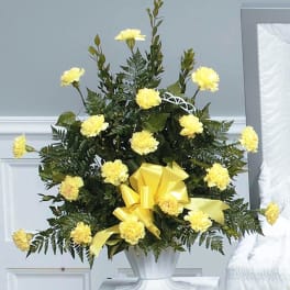 Tall arrangement of yellow carnations with a large yellow bow in a white urn vase