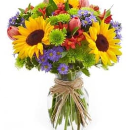 Colorful bouquet of sunflowers, tulips, and purple daisies in a glass vase