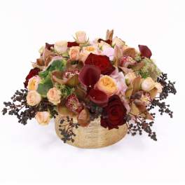 Low centerpiece of red and peach roses, burgundy calla lilies, and orchids in a gold vase