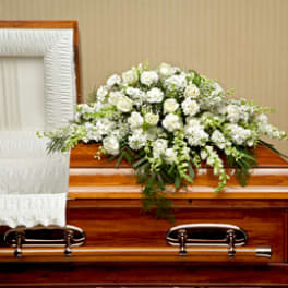 White floral spray on a wooden casket beside a white-lined interior
