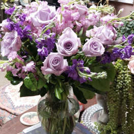 Lavender roses and purple flowers arranged in a clear glass vase