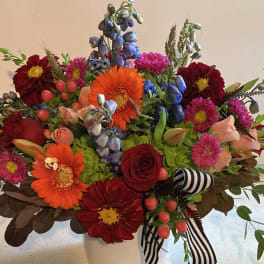 Mixed bouquet of bright flowers in a white vase with striped ribbon