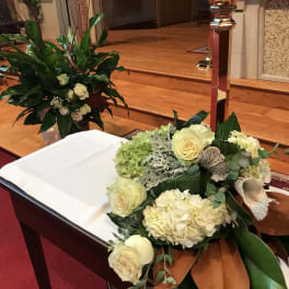 Cream floral arrangement on a church altar beside a white-draped casket