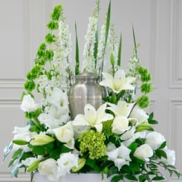 White lilies and roses arranged around a silver urn with green accents