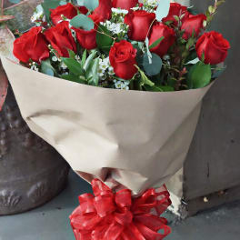 Hand-tied bouquet of red roses with small white flowers wrapped in kraft paper and tied with a red bow