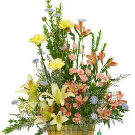 Tall basket arrangement with yellow lilies, carnations, peach spray roses, and pastel filler flowers