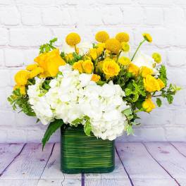 Yellow roses and white hydrangeas in a green square vase