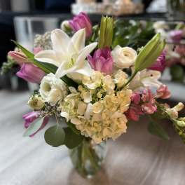 Mixed bouquet of white lilies, hydrangeas, and pink tulips in a clear glass vase