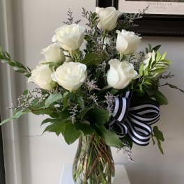 White roses arranged in a glass vase with a black-and-white ribbon