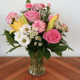 Pink roses, yellow lilies, and white daisies in a glass vase