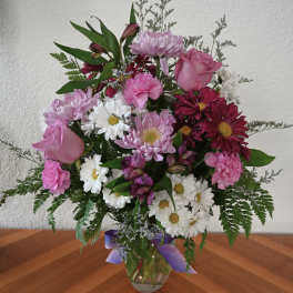 Mixed pink and white bouquet in a glass vase with a purple ribbon