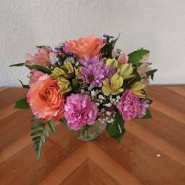 Mixed bouquet of roses, carnations, and daisies in a clear glass vase