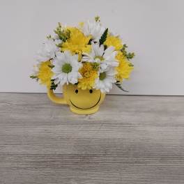Yellow and white daisy and mum arrangement in a yellow smiley face mug