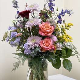 Mixed bouquet of pink roses, lavender blooms, and blue flowers in a glass vase