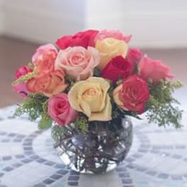 Round bouquet of red, pink, peach, and cream roses in a clear glass bowl vase