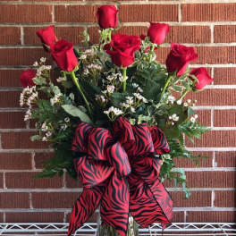 Red roses arranged in a clear glass vase with a large red-and-black ribbon