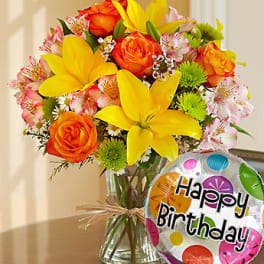 Bouquet of orange roses and yellow lilies in a glass vase with a birthday balloon