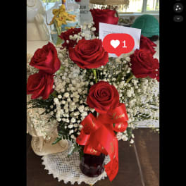 Arrangement of red roses and white filler flowers in a red glass vase with a red love ribbon