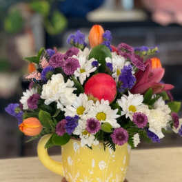 Mixed bouquet in a yellow mug with white daisies, purple blooms, and orange tulips