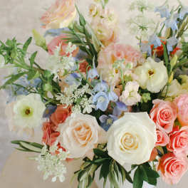 Pastel bouquet of roses, blue flowers, and white blooms in a white vase