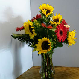 Bouquet of sunflowers and red gerbera daisies in a clear glass vase