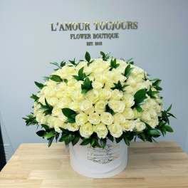 Large round hatbox of creamy white roses with dark green accents on a wooden table
