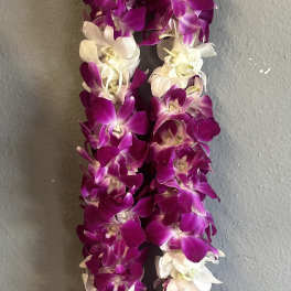 Purple and white orchid lei hanging against a gray wall