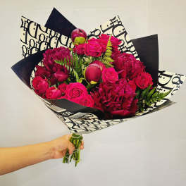 Handheld bouquet of hot pink roses and deep magenta blooms in patterned wrap