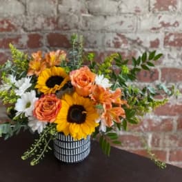Bouquet of sunflowers, orange roses, and white daisies in a striped vase
