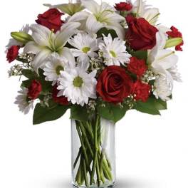 Red roses and white lilies with daisies in a clear glass vase