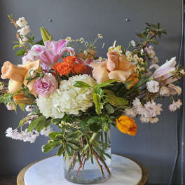 Mixed arrangement of peach roses, pink lilies, and white hydrangeas in a clear glass vase