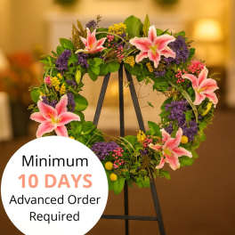 Standing wreath with pink lilies and mixed purple and yellow flowers on a black easel.