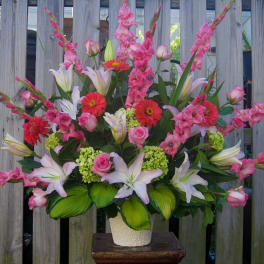 Tall bouquet of pink lilies, roses, and red gerbera daisies in a white vase
