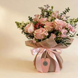 Pink rose and carnation arrangement with white accents in a burlap-wrapped pot tied with a pink satin bow