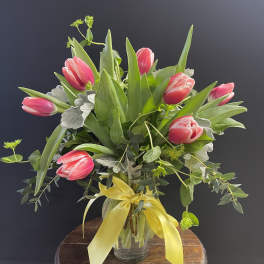 Pink tulips in a glass vase with a yellow ribbon