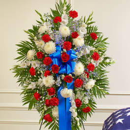 Standing floral spray with red, white, and blue flowers and a blue ribbon