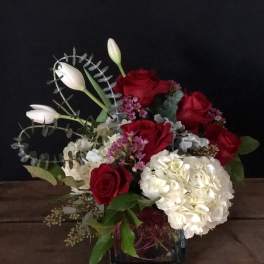 Red roses and white hydrangea in a glass vase with white tulips