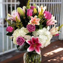 Bouquet of pink lilies, roses, and white hydrangeas in a glass vase