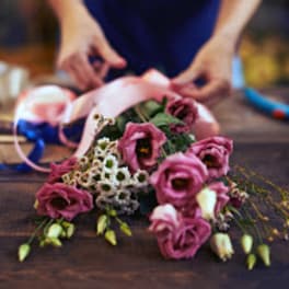 Pink flowers arranged on a table while hands tie ribbon around them.