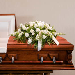 White floral spray on a wooden casket with ribbon accents