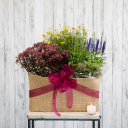 Mixed flowers in a burlap-wrapped basket with a pink ribbon and candle