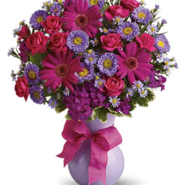 Pink and purple mixed flower bouquet in a lavender vase with a ribbon