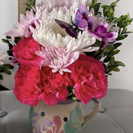 Pink and white flowers arranged in a painted ceramic mug with butterfly decorations.