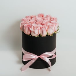 Pink roses arranged in a black round box with a pink ribbon