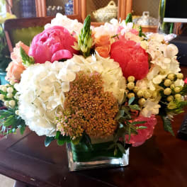 Mixed bouquet of pink, red, white, and peach flowers in a square glass vase
