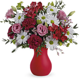 Mixed bouquet of white daisies, pink roses, and red flowers in a red vase