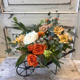 Mixed bouquet of orange, white, and blush roses with yellow blooms in a black wagon vase
