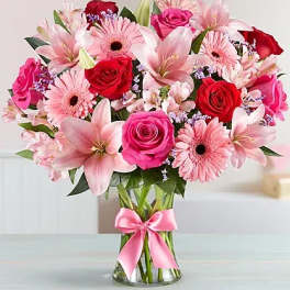 Pink and red bouquet of roses, lilies, and gerbera daisies in a glass vase