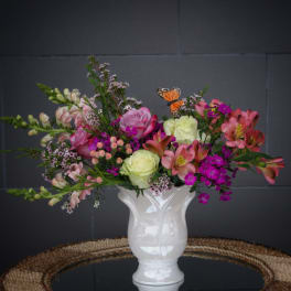 Mixed pink and white flowers in a white vase with a butterfly accent